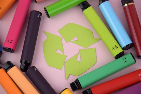 Mehrere-bunte-Vapes-und-E-Zigaretten-liegen-um-das-Recycling-Symbol